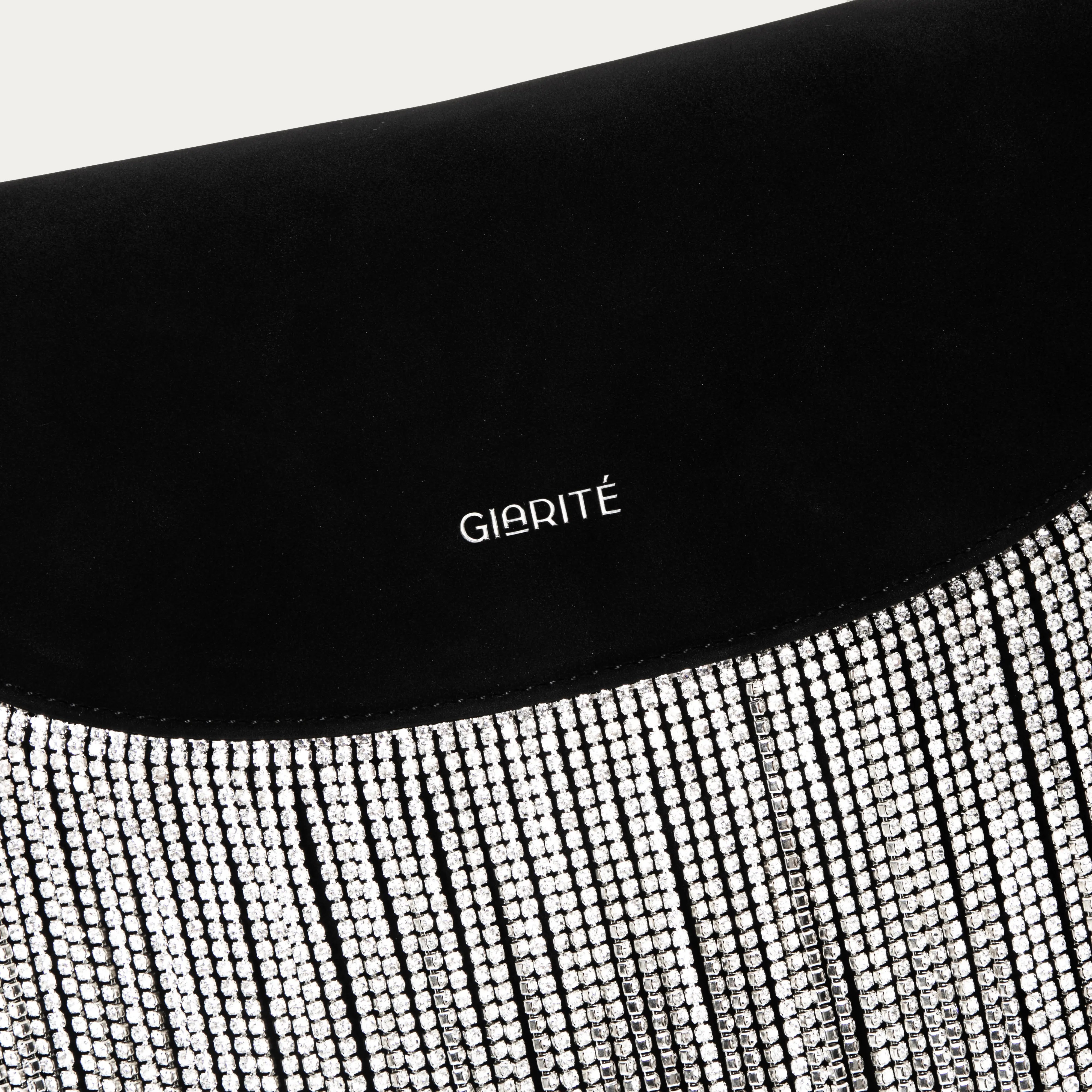 A close-up of a black Giarité Tina bag featuring a prominent fringe of sparkling, silver-toned embellishments and the brand name GIARITÉ in white text on the black vegan suede body.