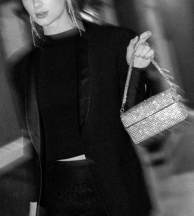 A black and white photo of a person wearing a dark outfit, holding Giarite's Rio Silver rhinestone-embellished clutch bag.