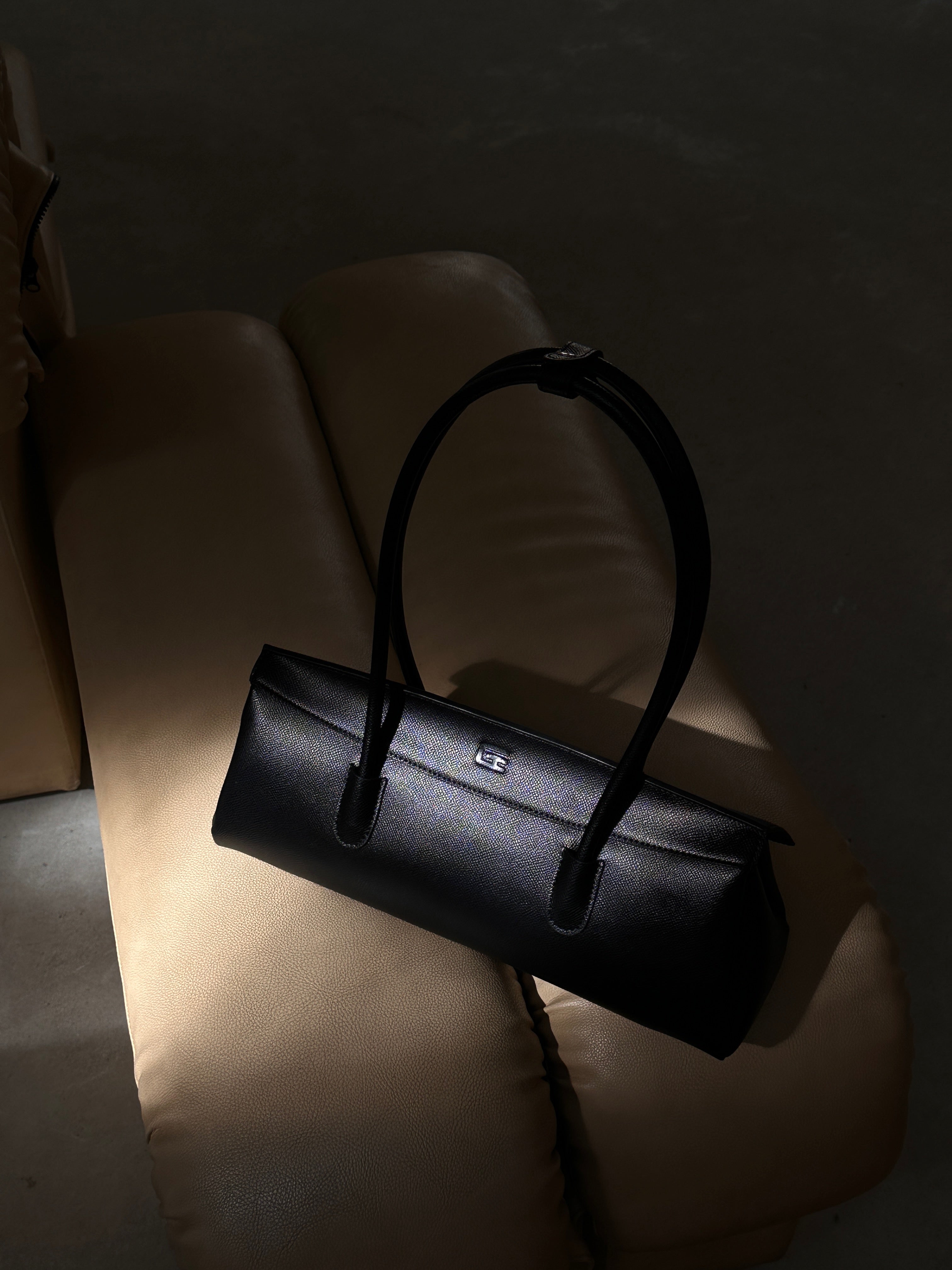 A black Giarité Valyn handbag with a structured, rectangular silhouette and a single top handle, resting on a light-colored surface with dramatic lighting highlighting the bag's form.