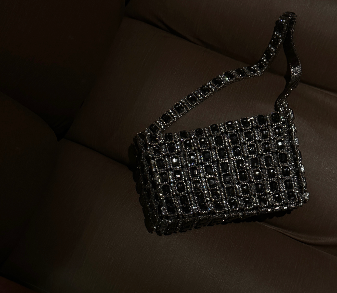 A close-up of Giarite's Rio bag, a small, dark-colored handbag adorned with shimmering embellishments and a chain strap.