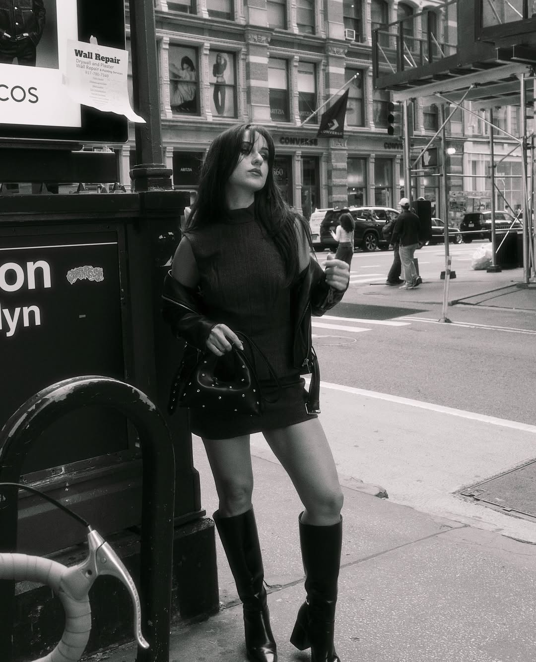 Black and white photo of a woman in a city street wearing a dress and boots.